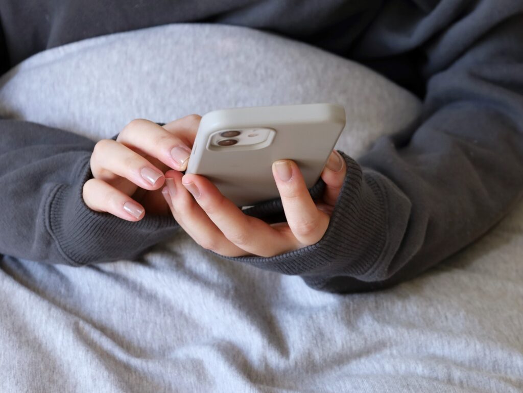 布団でスマホをいじる女性の画像
