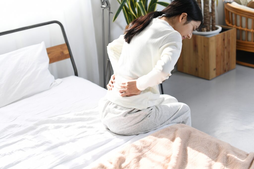 ベッドの上で腰が痛そうな女性の画像